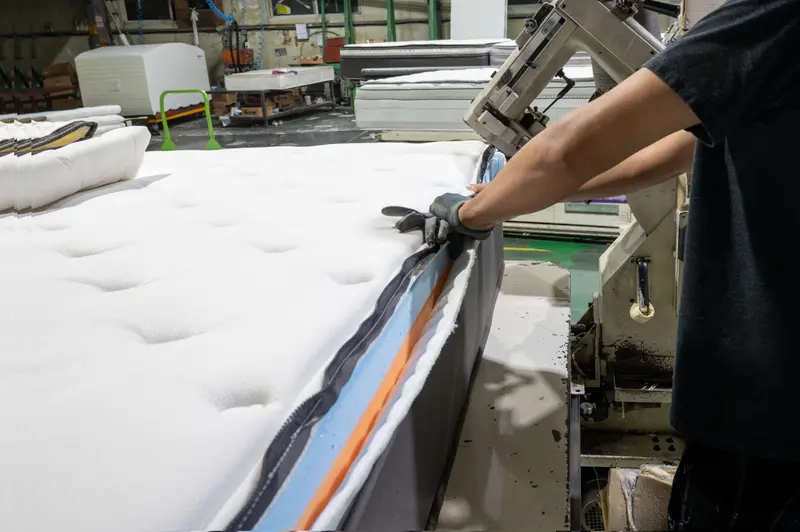 A TFM operator guiding a mattress edge through the tape-edge sewing machine